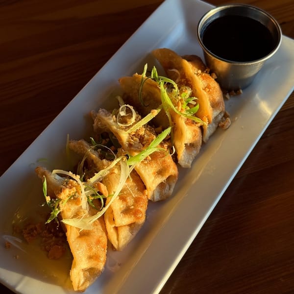 Fried dumplings garnished with green onions and peanuts, served with a side of dark dipping sauce.