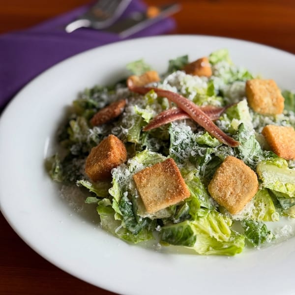 Caesar salad with romaine lettuce, croutons, anchovies, and grated Parmesan cheese on a white plate.