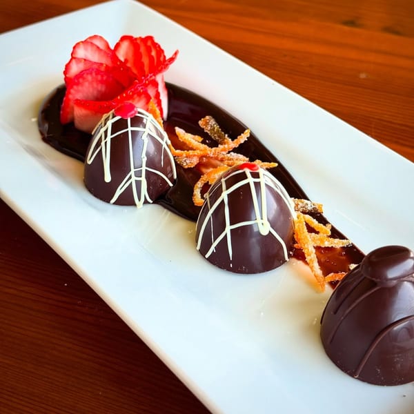 Three chocolate desserts with white icing, strawberries, and candied orange peel on a white plate.