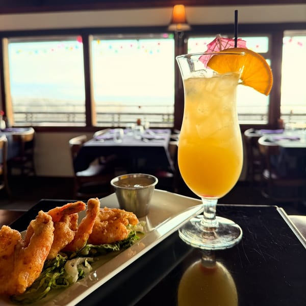 Fried shrimp and a tropical drink with an orange slice and umbrella, overlooking the ocean.