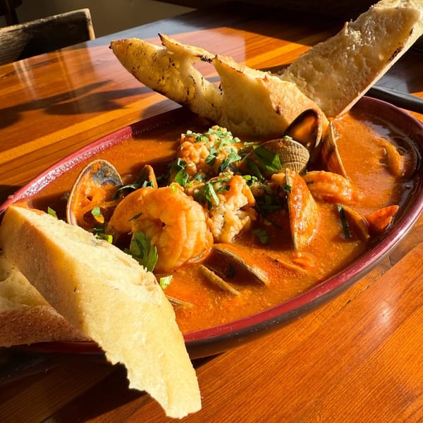 Seafood cioppino with shrimp, clams, and mussels in a rich broth, garnished with parsley and baguette.