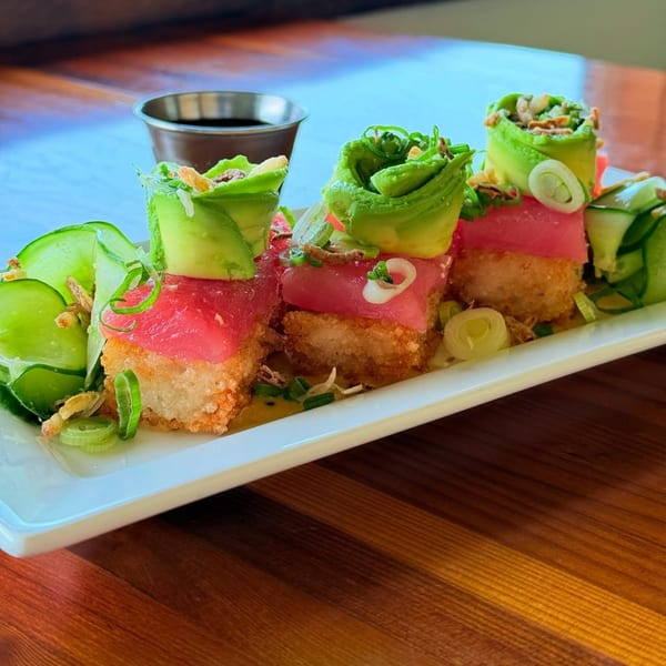 Three fried rice squares topped with tuna, avocado, and green onions, with a side of soy sauce.
